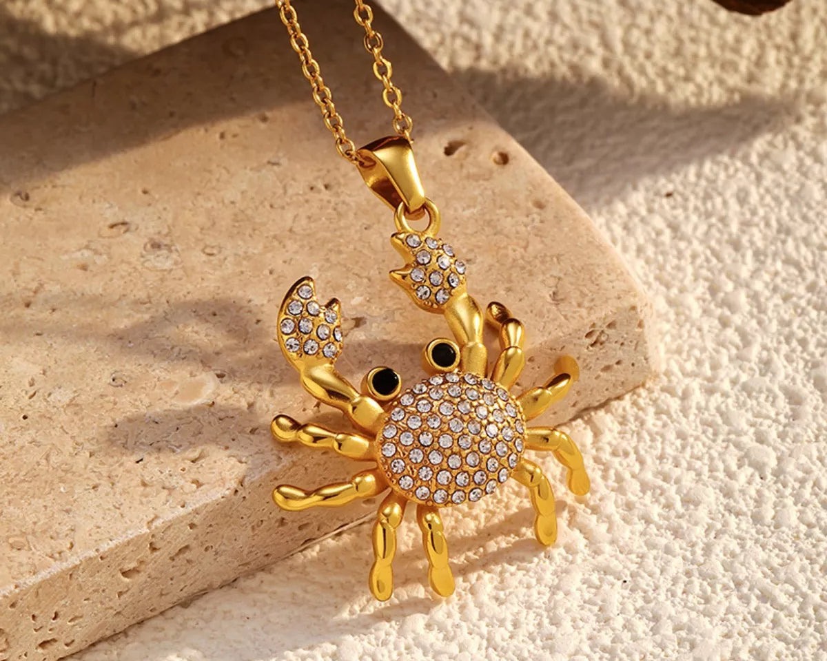 NYLD Glamour Collection by NEWYORKLISTED: Gold crab-shaped pendant with rhinestones on a beige stone surface