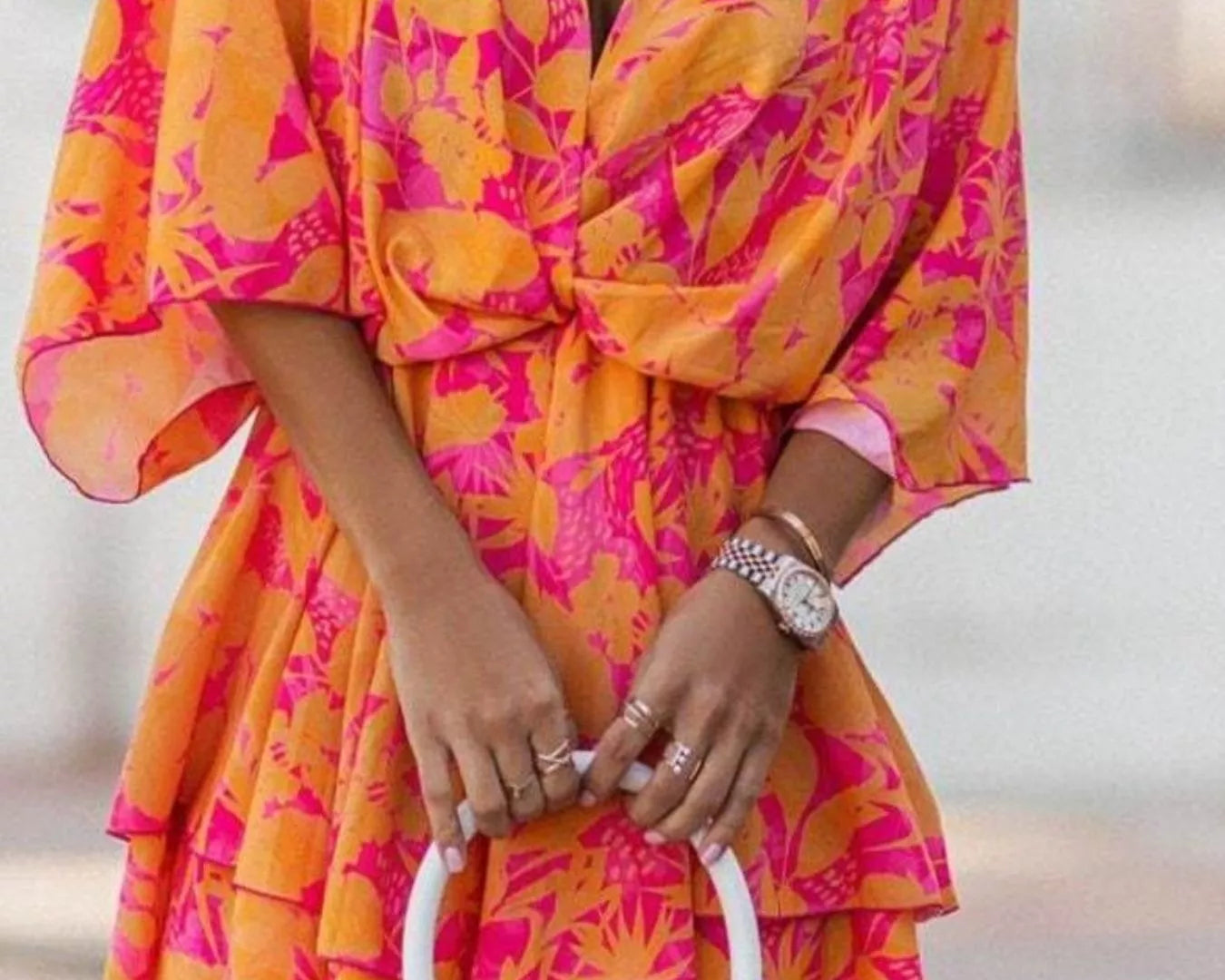 NEWYORKLISTED STYLE COLLECTION: Person wearing a bright orange and pink floral dress holding a white handbag.