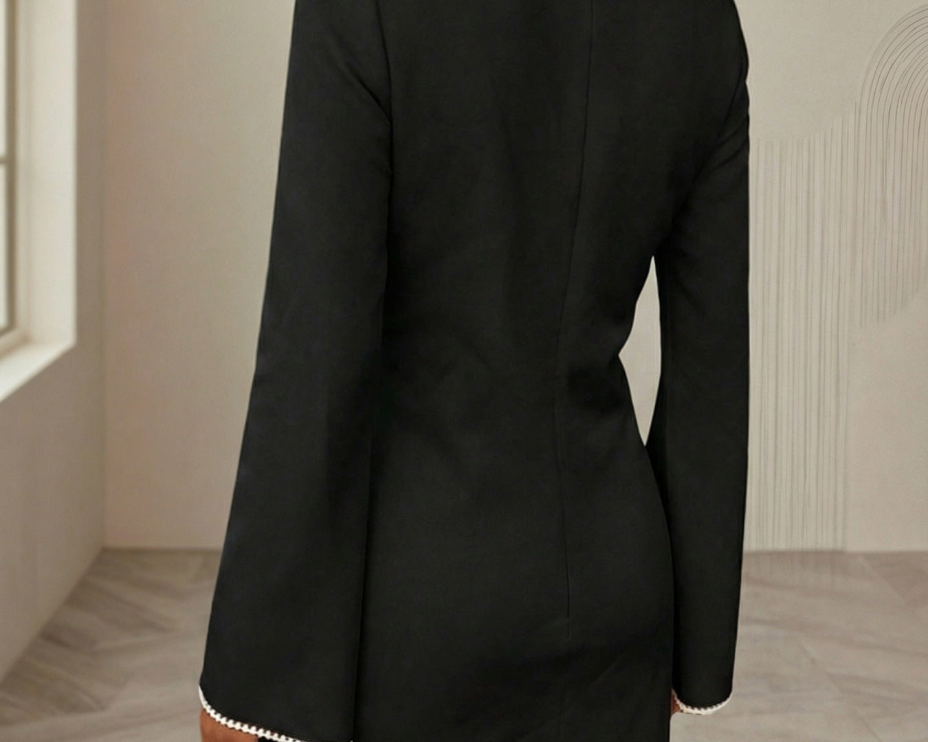 NEWYORKLISTED STYLE COLLECTION: Person wearing a black dress with white trim in a neutral setting