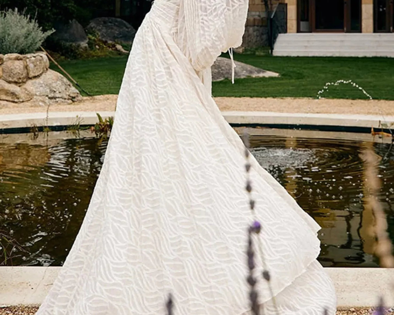 NEWYORKLISTED STYLE COLLECTION: Woman in a white dress standing by a pond with trees and a building in the background