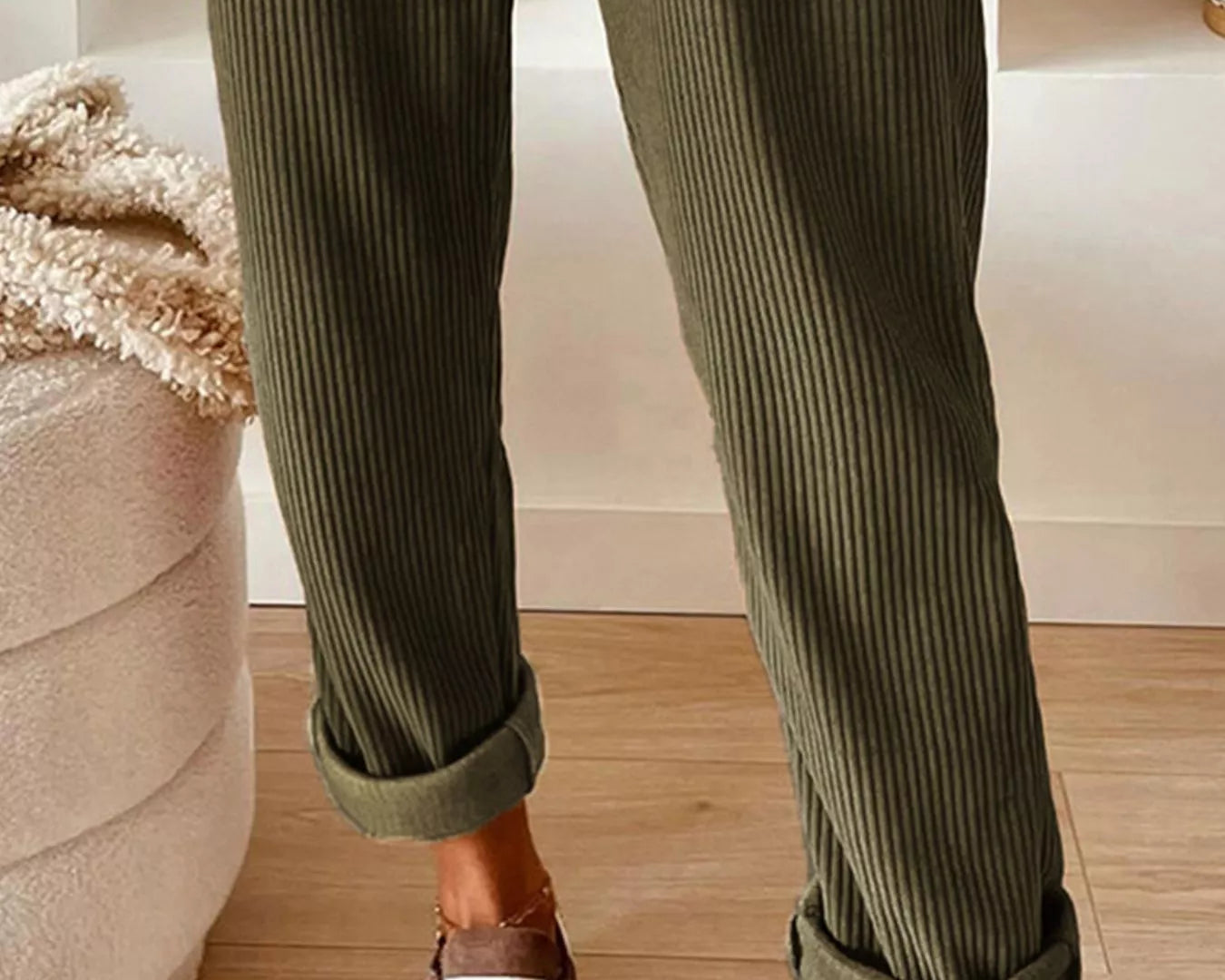 Person wearing green ribbed pants with white sneakers in a home setting