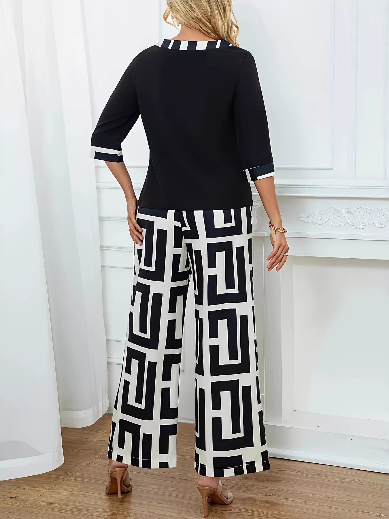 NEWYORKLISTED STYLE COLLECTION: Woman wearing a black top and geometric-patterned pants in a room with white curtains and a fireplace.