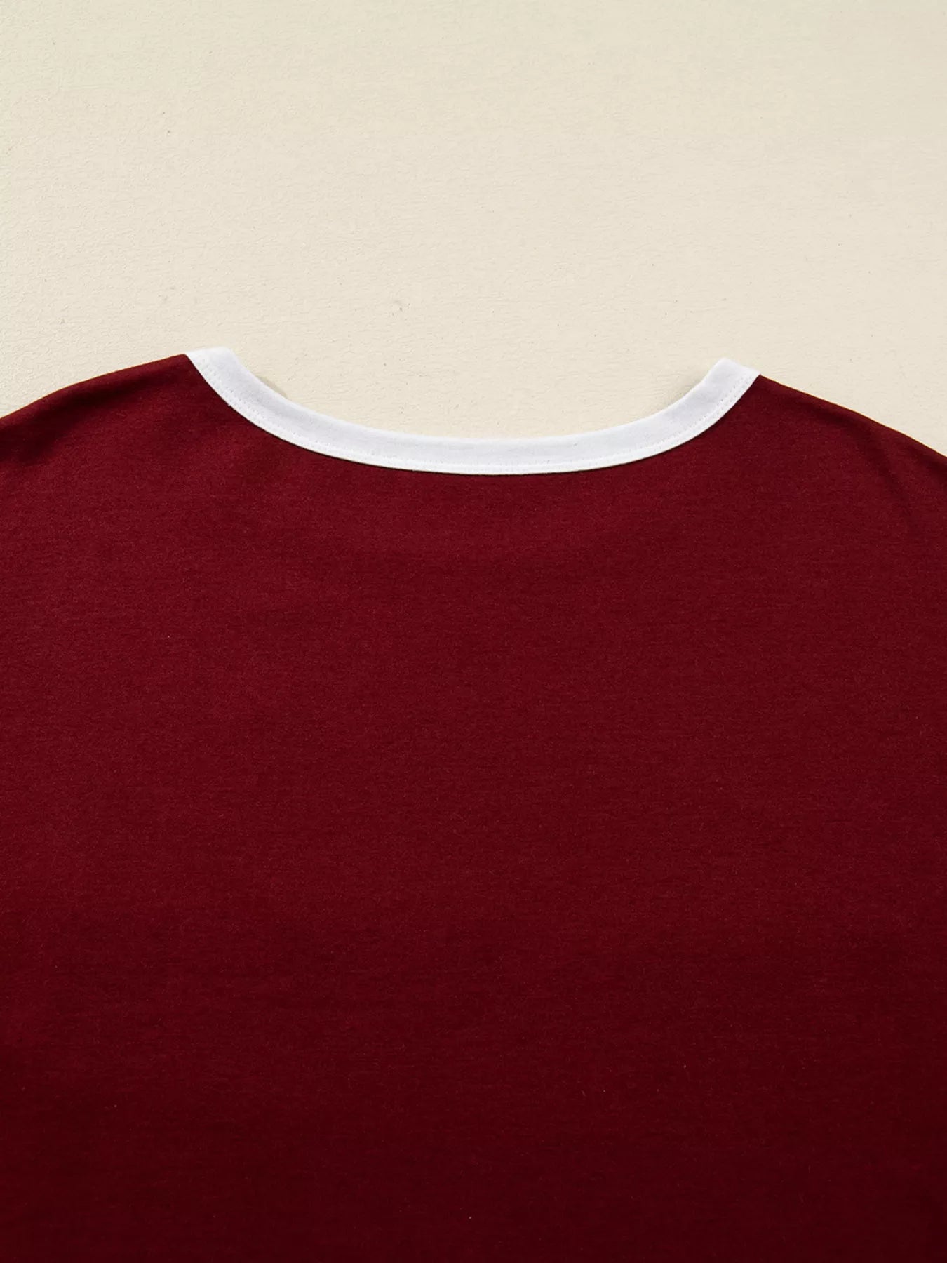 Close-up of a maroon shirt with white trim on a beige background