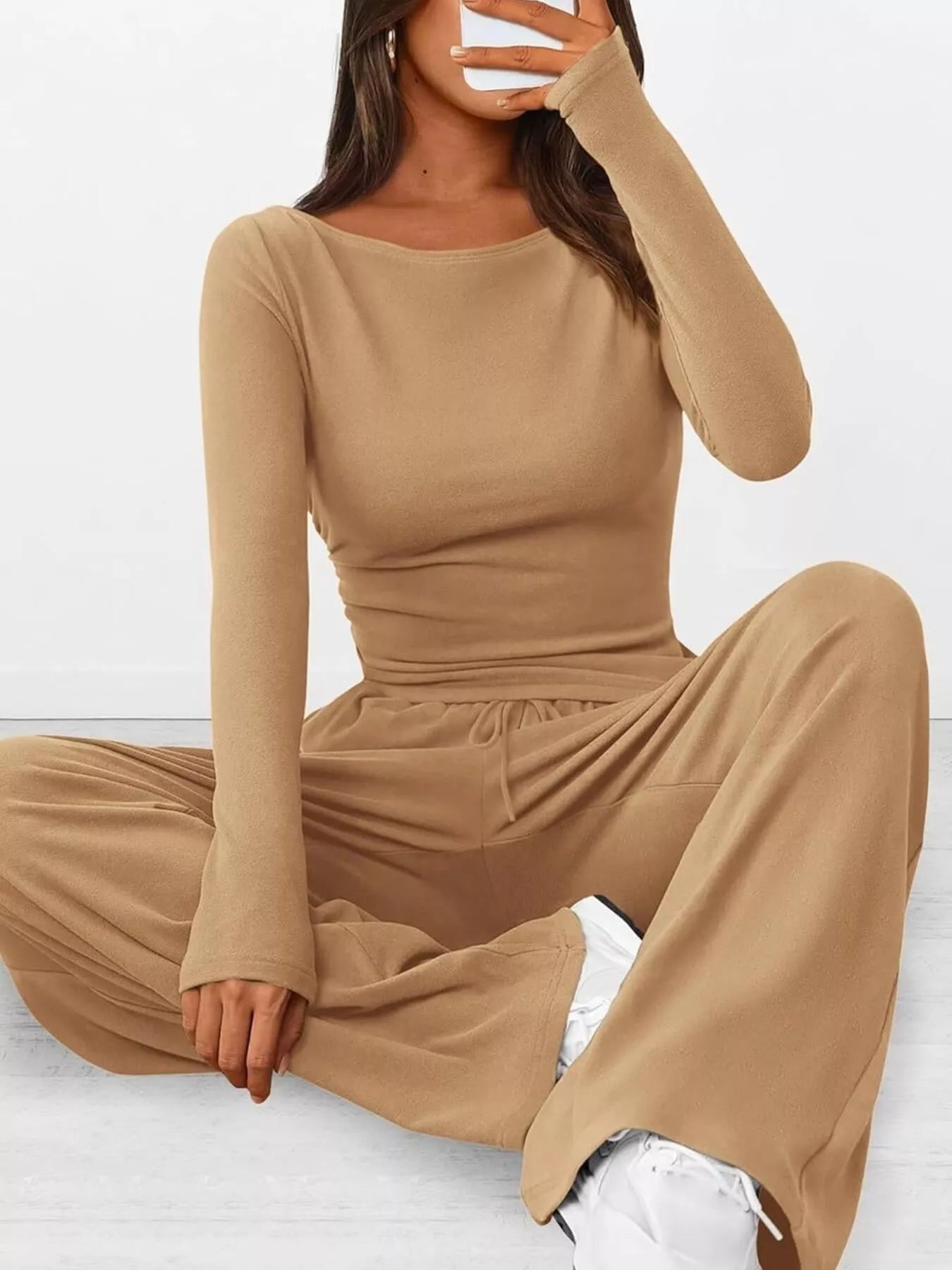 Person wearing a beige long-sleeve top and wide-leg pants on a white background