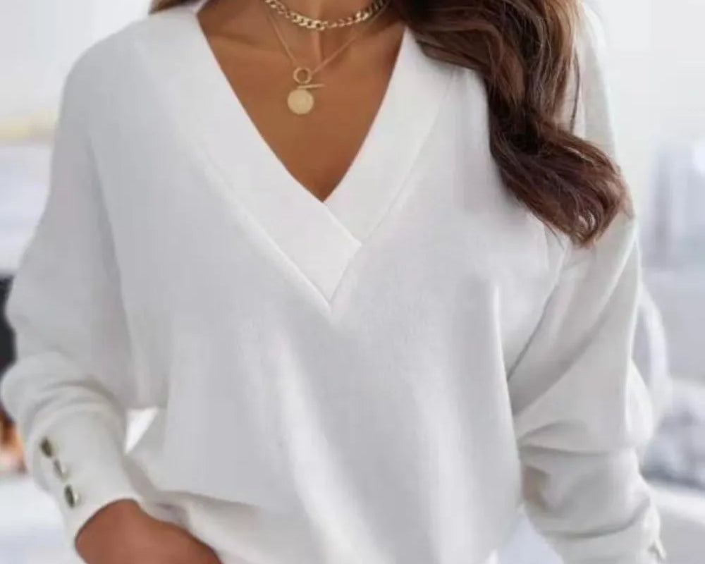 NEWYORKLISTED STYLE COLLECTION: Woman wearing a white long-sleeve top with a V-neckline, gold necklaces, and beige pants.