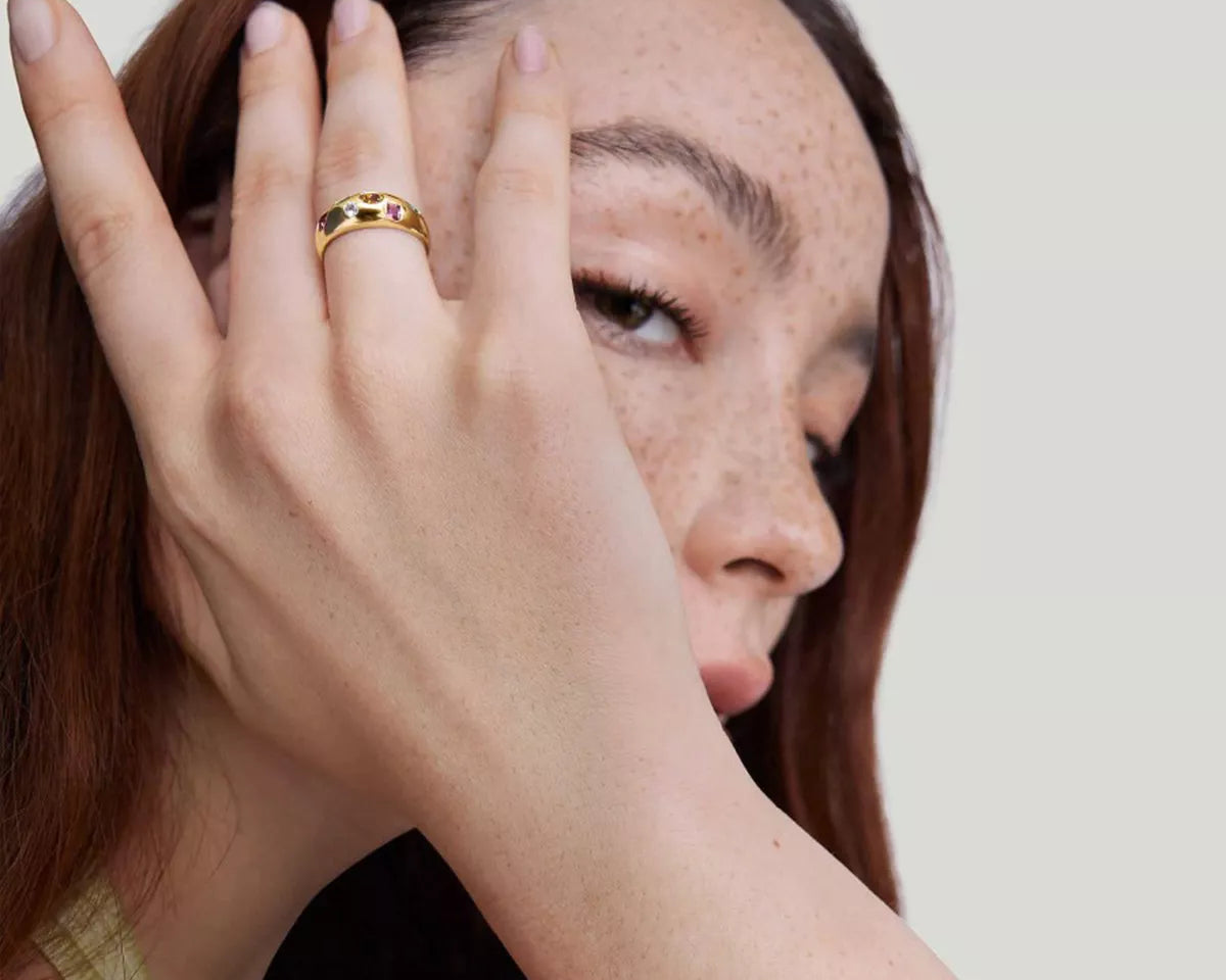 NYLD Glamour Collection by NEWYORKLISTED: Woman with freckles on her face wearing a gold ring, against a plain background