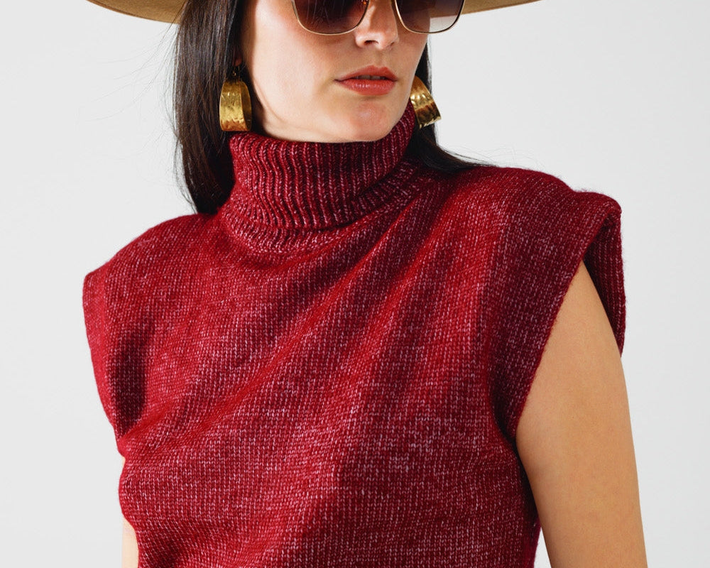 Woman wearing a red sleeveless sweater, tan hat, and sunglasses on a white background