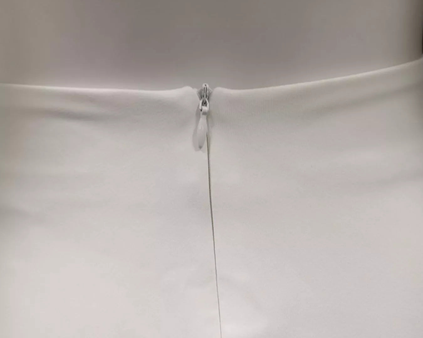 NEWYORKLISTED STYLE COLLECTION: Close-up of a white dress with a zipper on a plain background