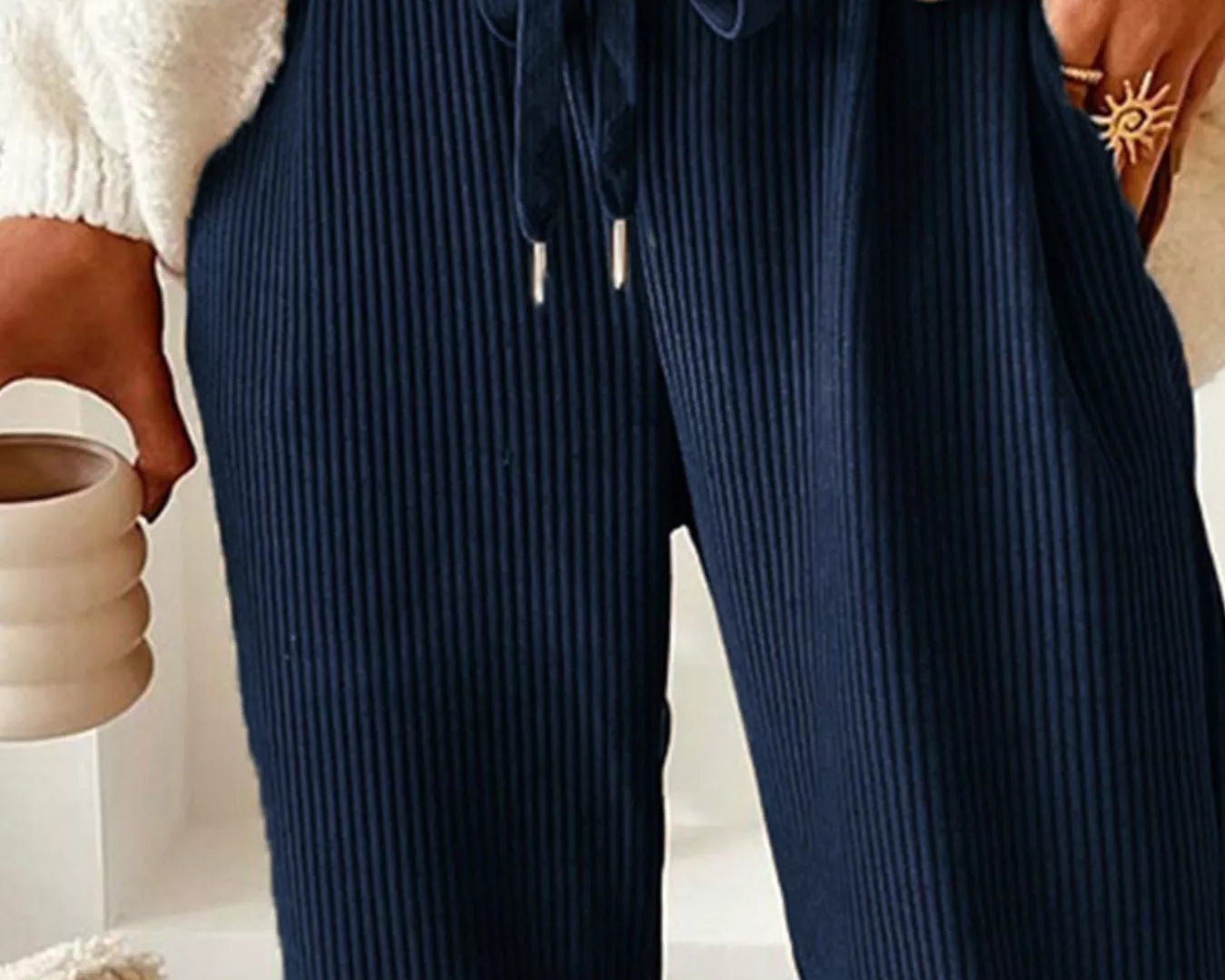 NEWYORKLISTED STYLE COLLECTION: Navy ribbed pants worn with a white sweater, held by a person.