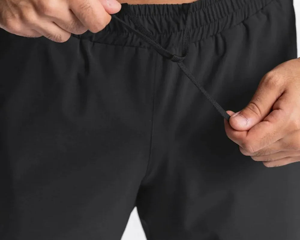 NEWYORKLISTED ATLAS MEN'S COLLECTION: Person adjusting the waistband of black shorts on a plain background