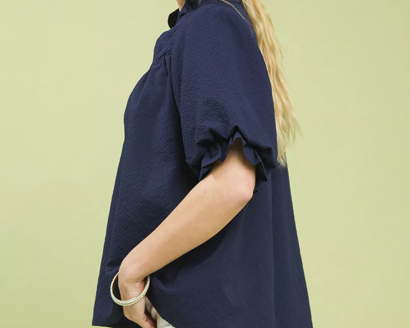 NEWYORKLISTED STYLE COLLECTION: Woman wearing a navy blue blouse with ruffled sleeves on a light green background