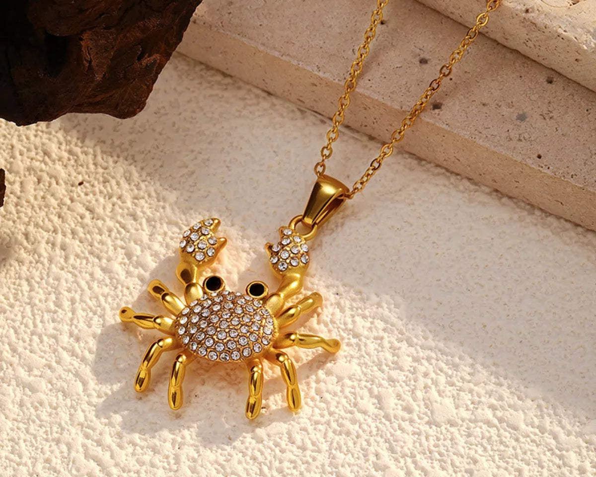 NYLD Glamour Collection by NEWYORKLISTED: Gold crab-shaped pendant with gemstones on a beige surface