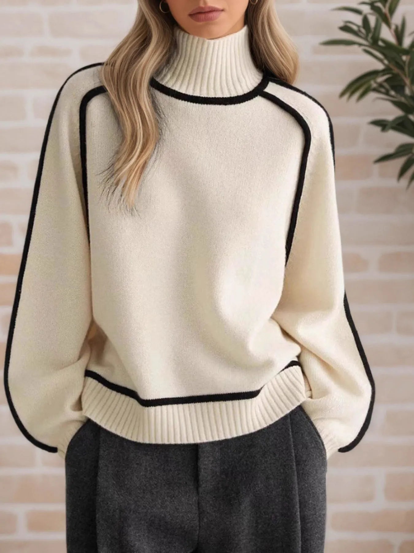 NEWYORKLISTED STYLE COLLECTION: Person wearing a cream sweater with black trim against a brick wall.