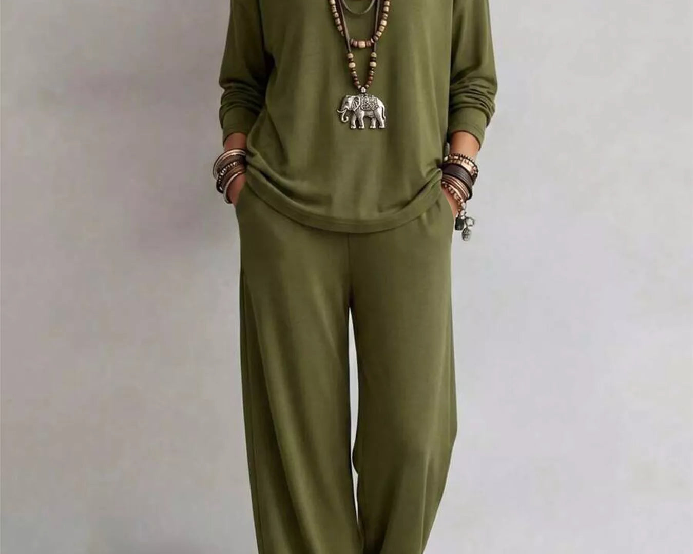 NEWYORKLISTED STYLE COLLECTION: A woman modeling a matching olive green lounge set consisting of a long-sleeve top and wide-leg pants, styled with layered necklaces and bracelets against a plain light gray background.