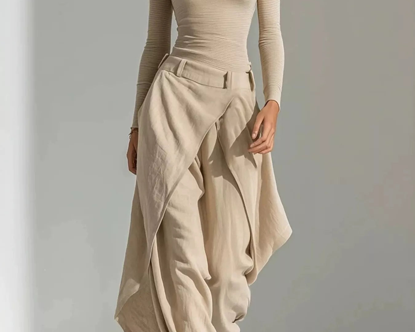 NEWYORKLISTED STYLE COLLECTION: A woman modeling a beige off-the-shoulder long-sleeve top paired with matching draped high-waisted maxi pants, styled with brown strappy sandals against a minimalist light gray studio background.