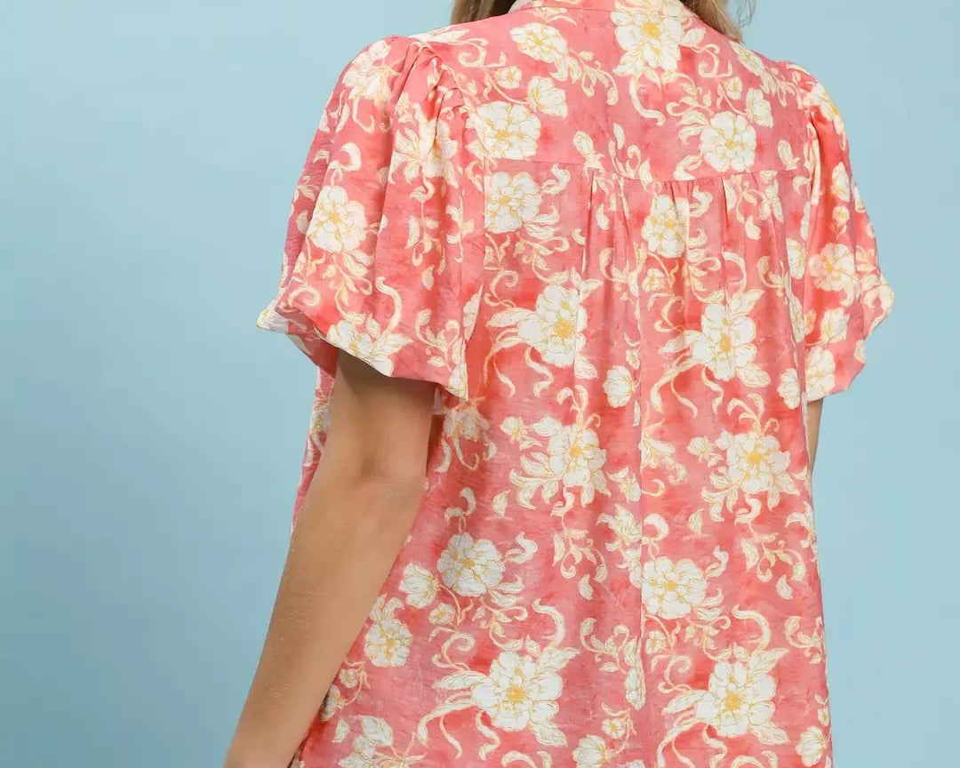 NEWYORKLISTED STYLE COLLECTION: Woman wearing a floral pink blouse with ruffled sleeves on a light blue background