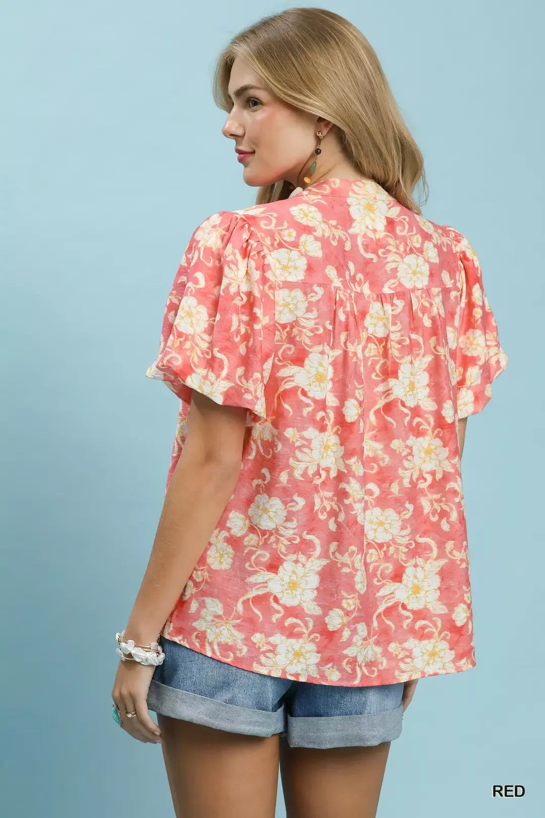 NEWYORKLISTED STYLE COLLECTION: Woman wearing a floral pink blouse with ruffled sleeves on a light blue background