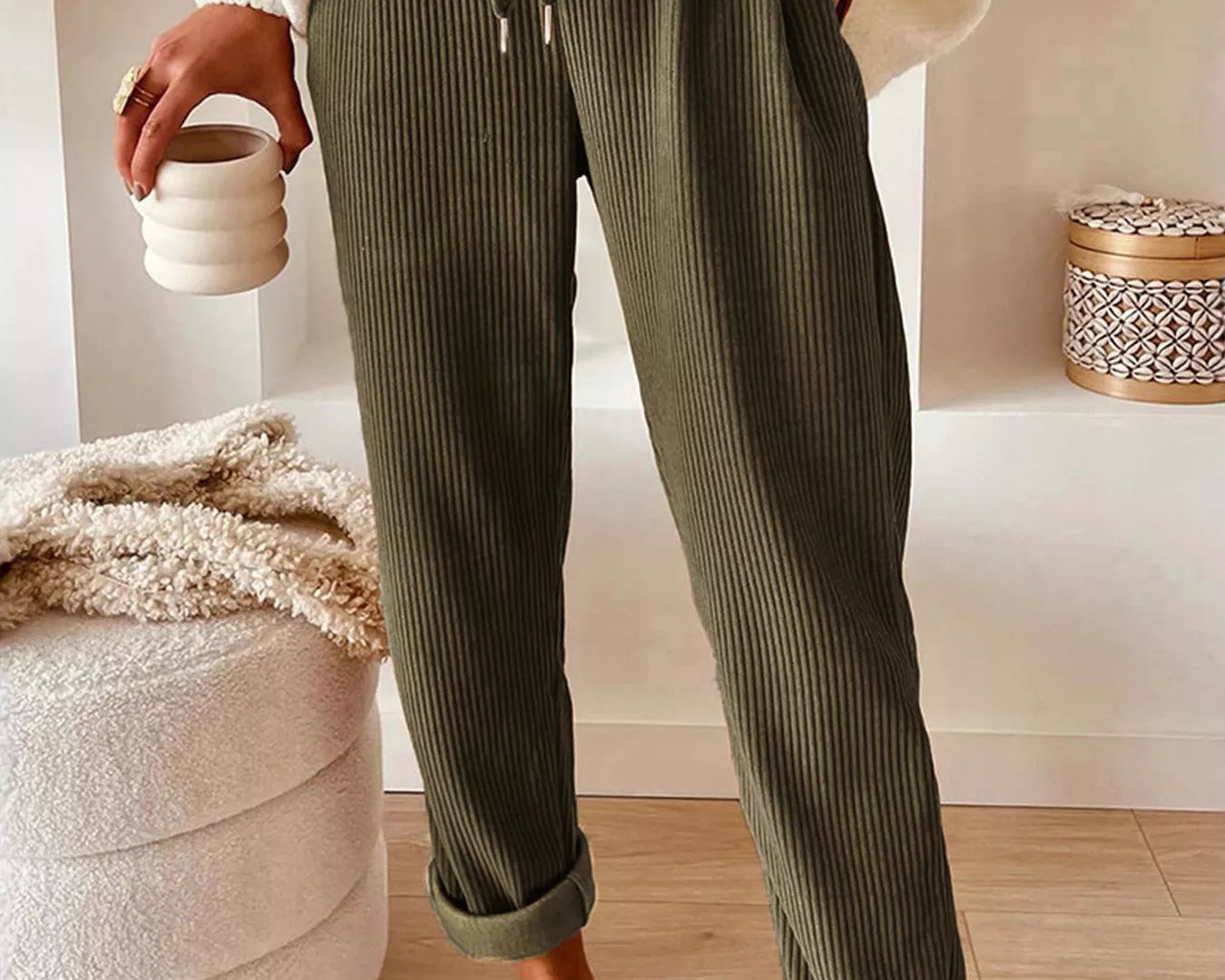 NEWYORKLISTED STYLE COLLECTION: Person wearing green ribbed pants with a white sweater and brown shoes, holding a cup.