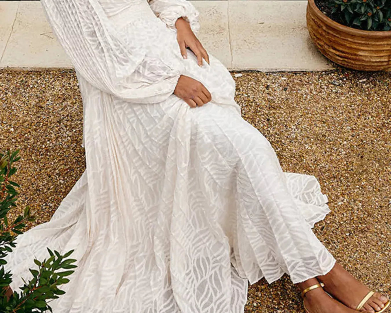 NEWYORKLISTED STYLE COLLECTION: Woman in a white lace dress sitting outdoors near a body of water.