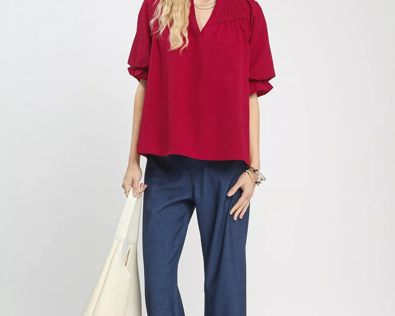 NEWYORKLISTED Style Collection: Woman wearing a red blouse and blue pants holding a white bag on a white background