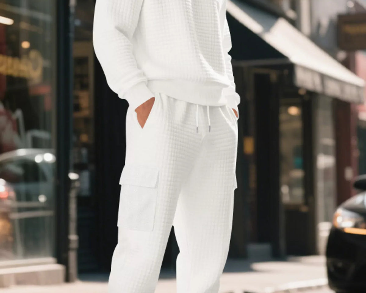 NEWYORKLISTED ATLAS MEN'S COLLECTION: A man wearing a white textured waffle-knit sweatshirt and matching cargo jogger pants, standing on a city street.
