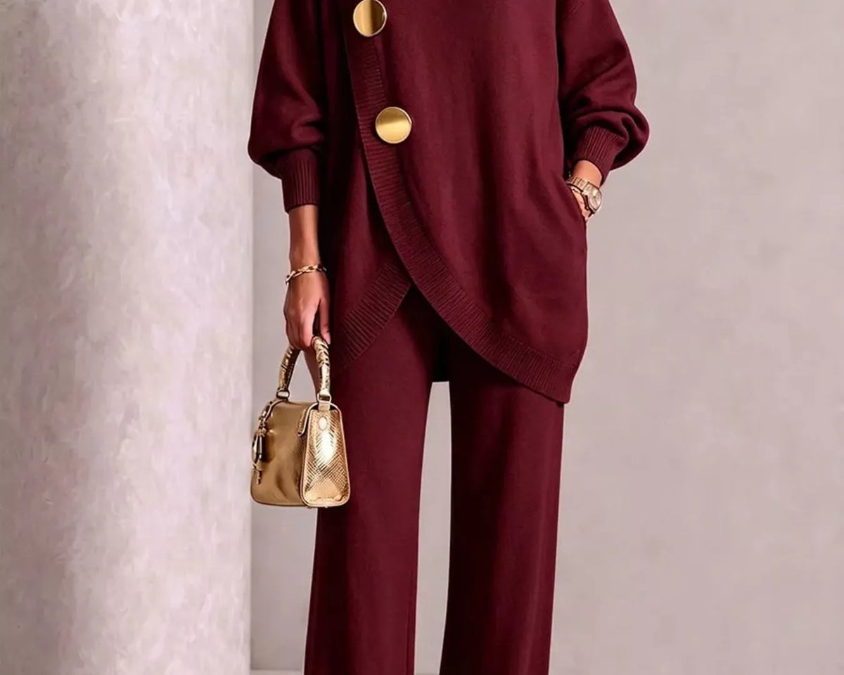 NEWYORKLISTED STYLE COLLECTION: A model wears a matching burgundy knit turtleneck sweater and wide-leg trousers set with large gold-tone decorative buttons. She is holding a small metallic gold handbag and wearing gold pointed shoes, set against a neutral textured studio backdrop.