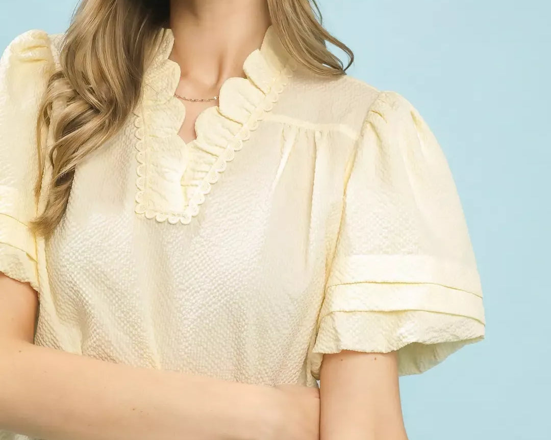 NEWYORKLISTED Style Collection: Woman wearing a cream-colored dress with ruffled sleeves against a light blue background