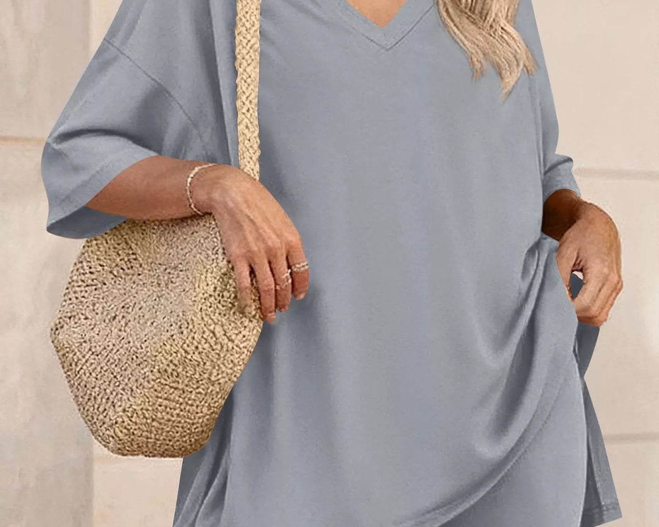 NEWYORKLISTED COMFORT COLLECTION: Woman wearing a gray outfit with a straw bag against a neutral background