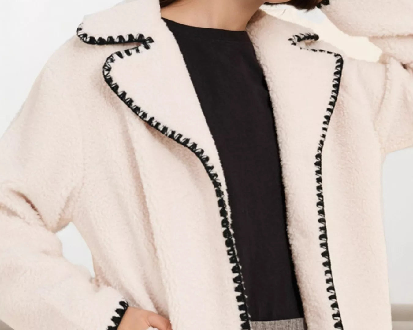 NEWYORKLISTED STYLE COLLECTION: Woman wearing a cream-colored jacket with black trim on a neutral background
