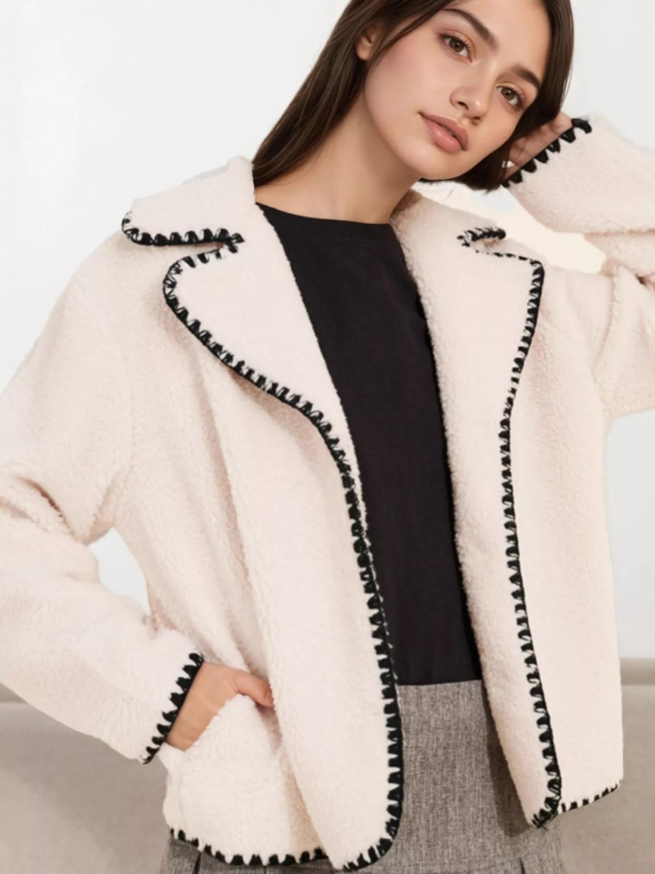 NEWYORKLISTED STYLE COLLECTION: Woman wearing a cream-colored jacket with black trim on a neutral background
