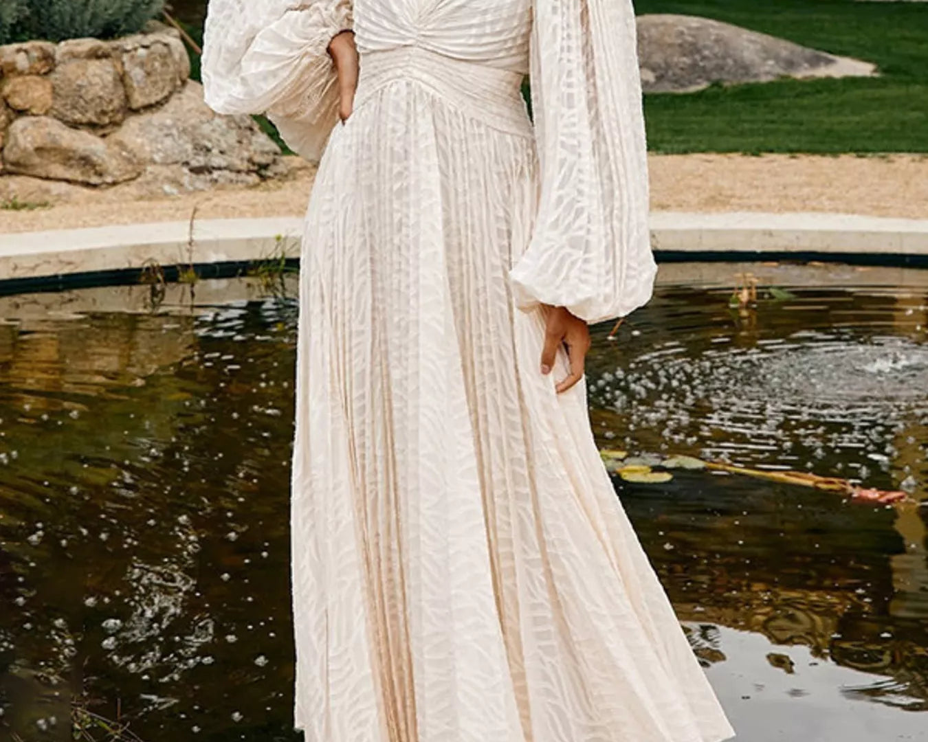 NEWYORKLISTED STYLE COLLECTION: Woman in a white lace dress standing by a pond with greenery in the background