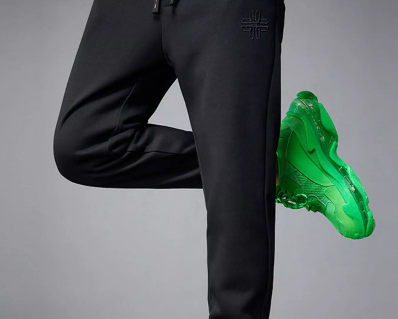 NEWYORKLISTED ATLAS MEN's COLLECTION: Person wearing black jogger pants and green sneakers on a gray background