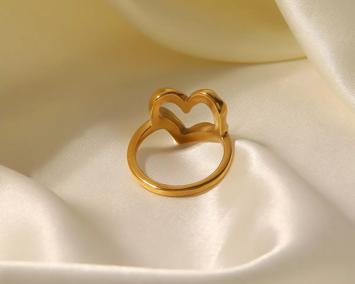 NYLD Glamour Collection by NEWYORKLISTED: Gold heart-shaped ring on a soft beige fabric background