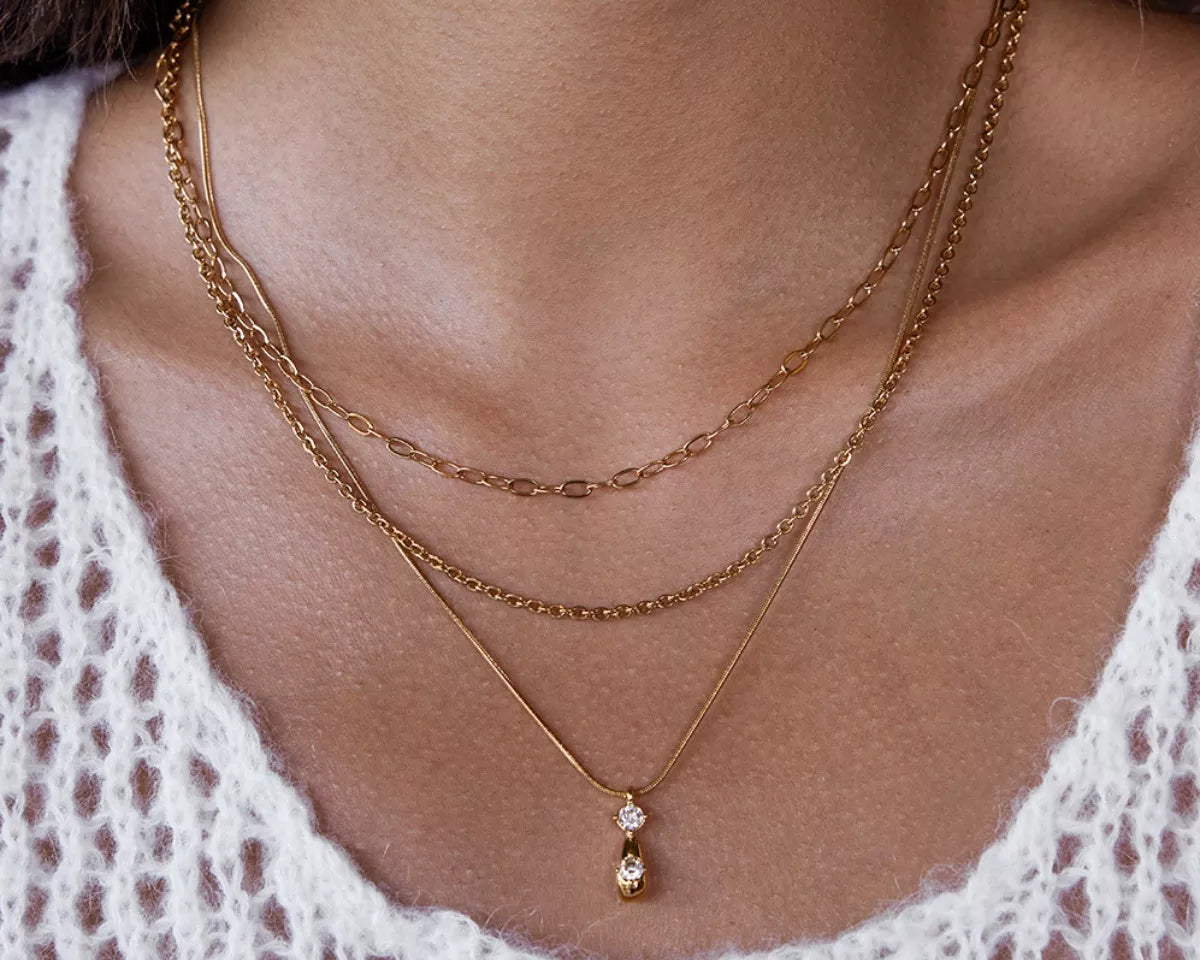 NYLD Glamour Collection by NEWYORKLISTED: Close-up of a person wearing a gold necklace with a pendant, layered with another necklace.
