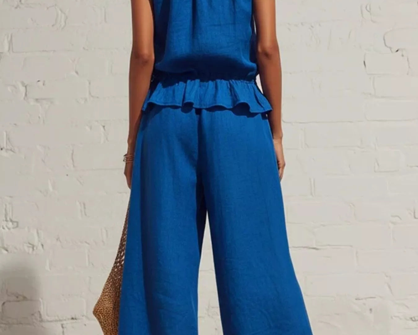 NEWYORKLISTED STYLE COLLECTION: Woman wearing a blue jumpsuit against a white brick wall.
