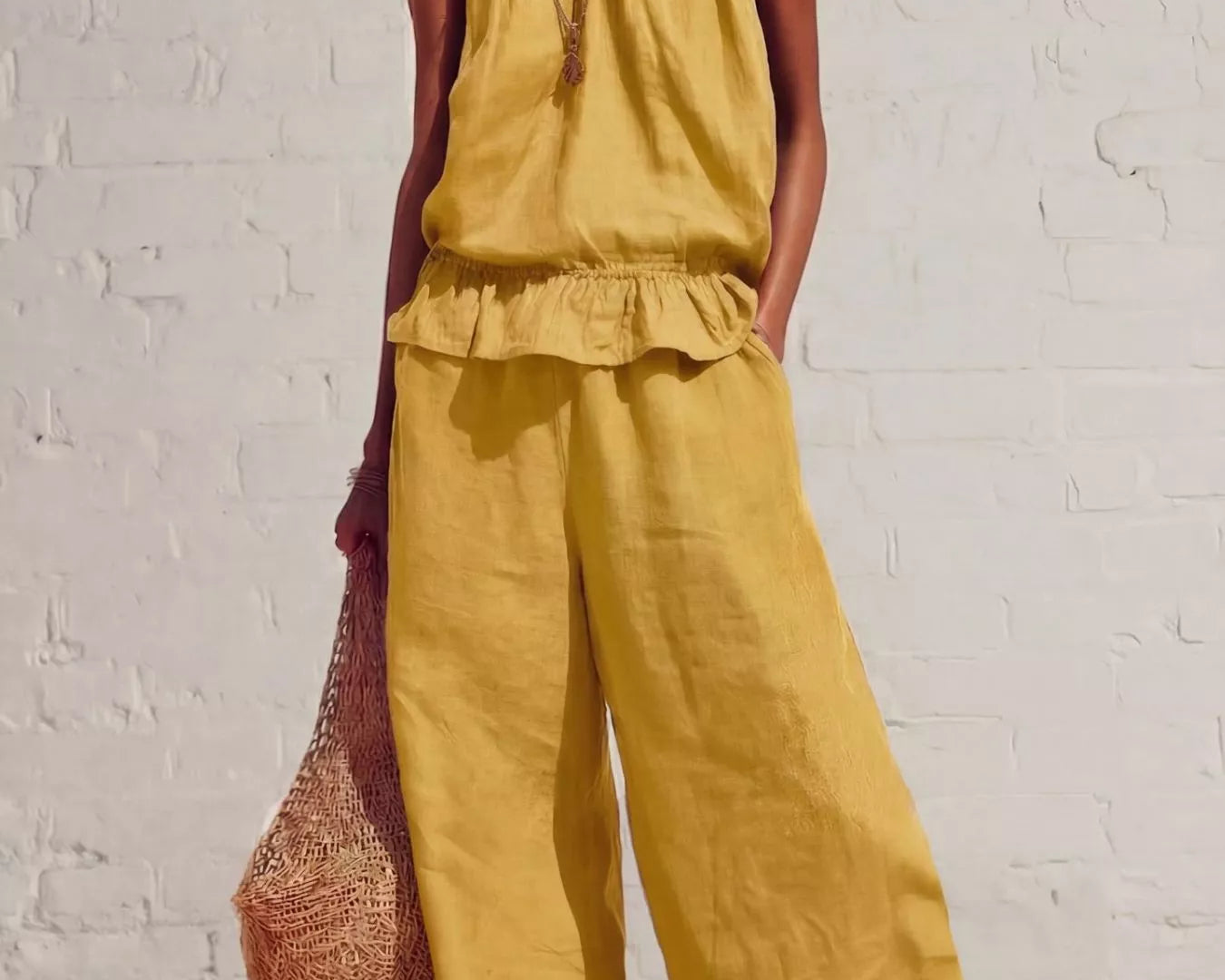 NEWYORKLISTED STYLE COLLECTION: Woman wearing a yellow outfit with wide-leg pants against a white brick wall.