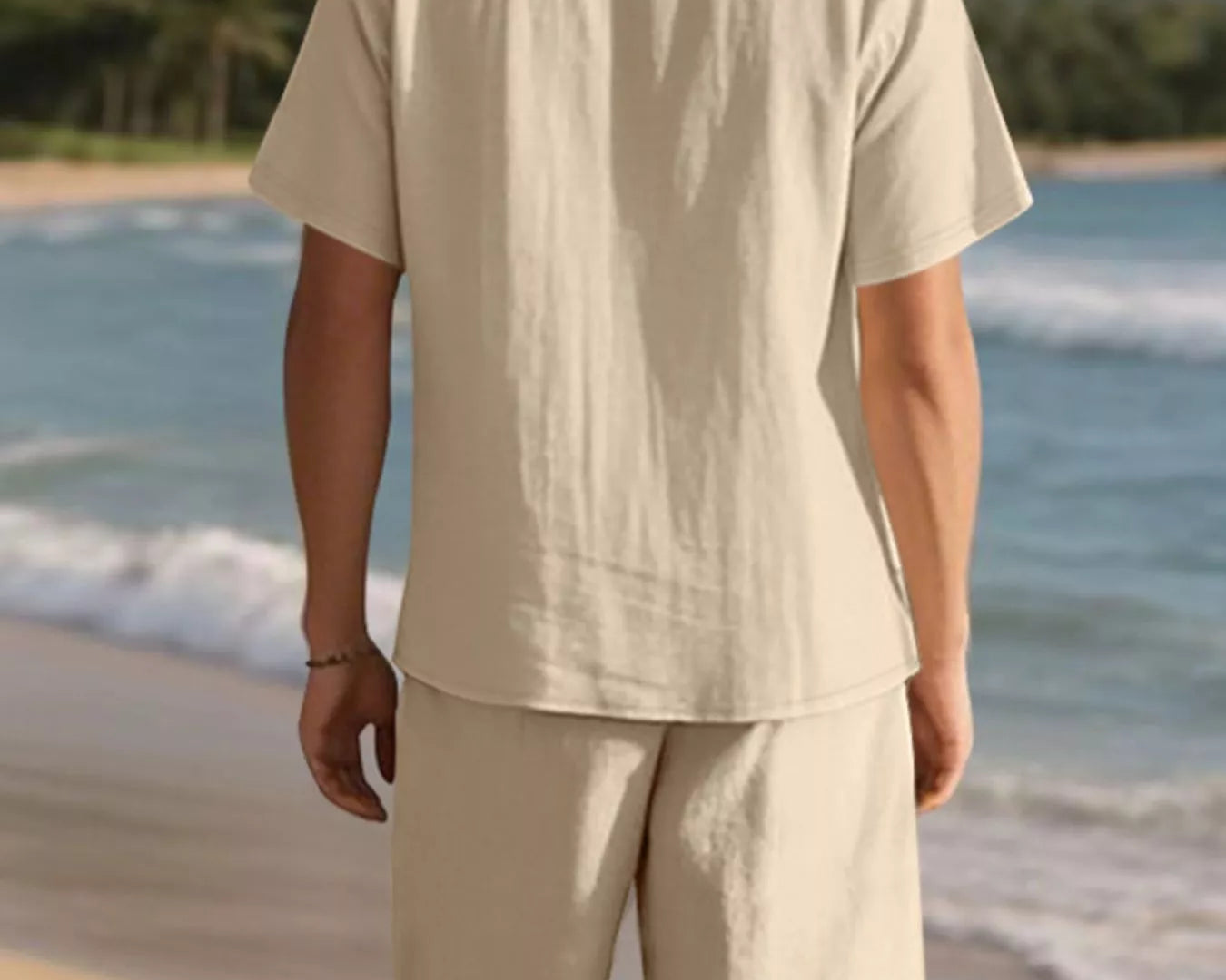 NEWYORKLISTED ATLAS MEN'S COLLECTION: Man in beige shirt and shorts standing on a beach with mountains in the background