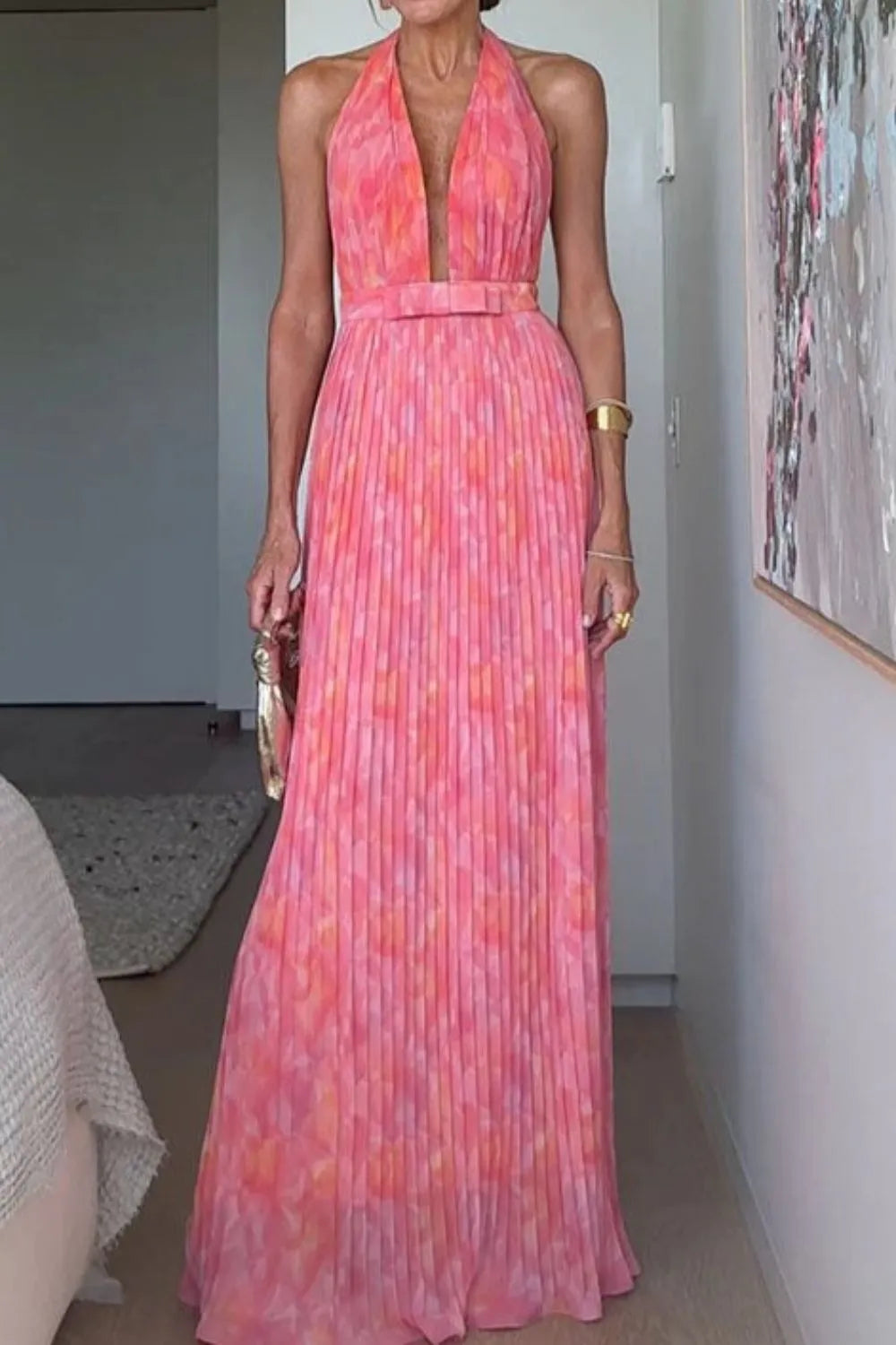 A flowing coral and pink halter neck pleated maxi dress with belted waist and backless design, perfect for summer weddings or resort evenings.
