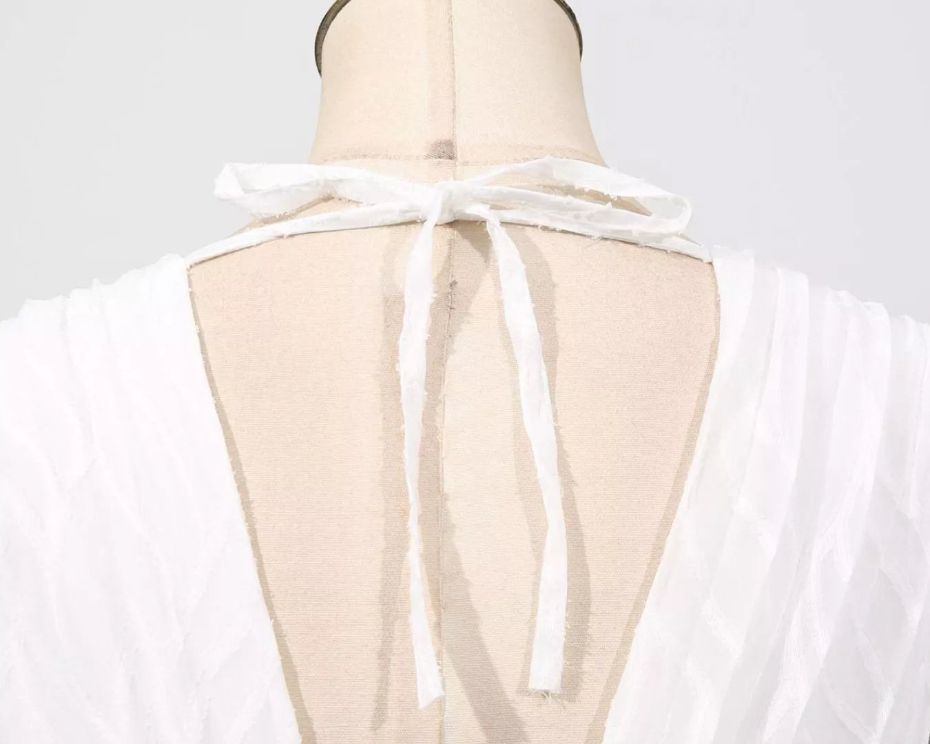 NEWYORKLISTED STYLE COLLECTION: White sheer top on a mannequin with a gold top against a white background