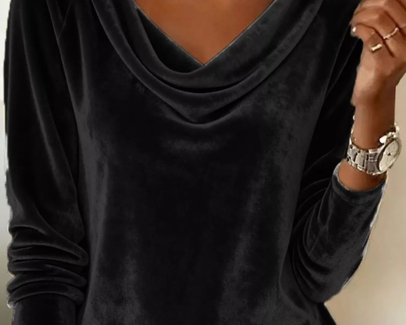 Person wearing a black long-sleeve top with a V-neckline, gold necklace, and watch on a neutral background.