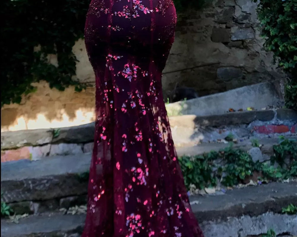 Person wearing a sparkly burgundy dress on stone steps with greenery in the background