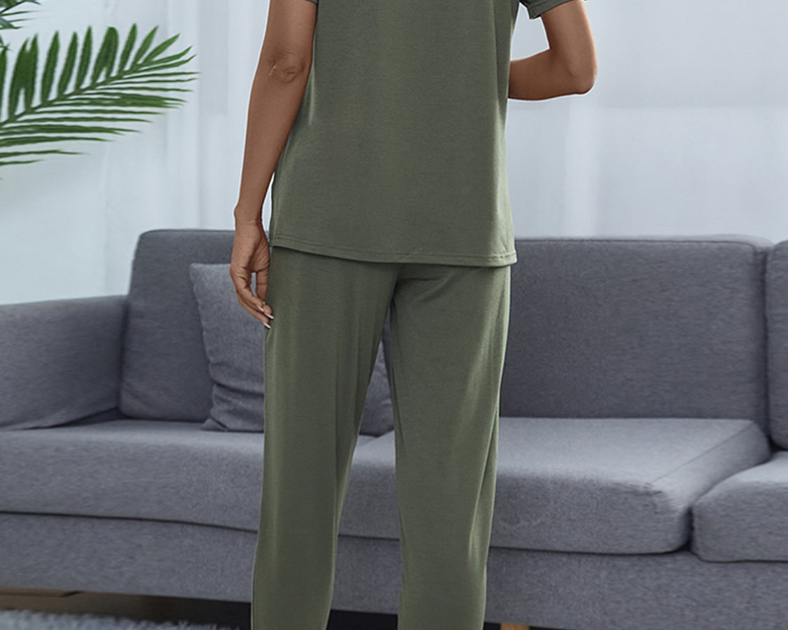 NEWYORKLISTED Intimate Apparel: Person wearing olive green pajamas standing in a living room with a gray sofa and white walls.