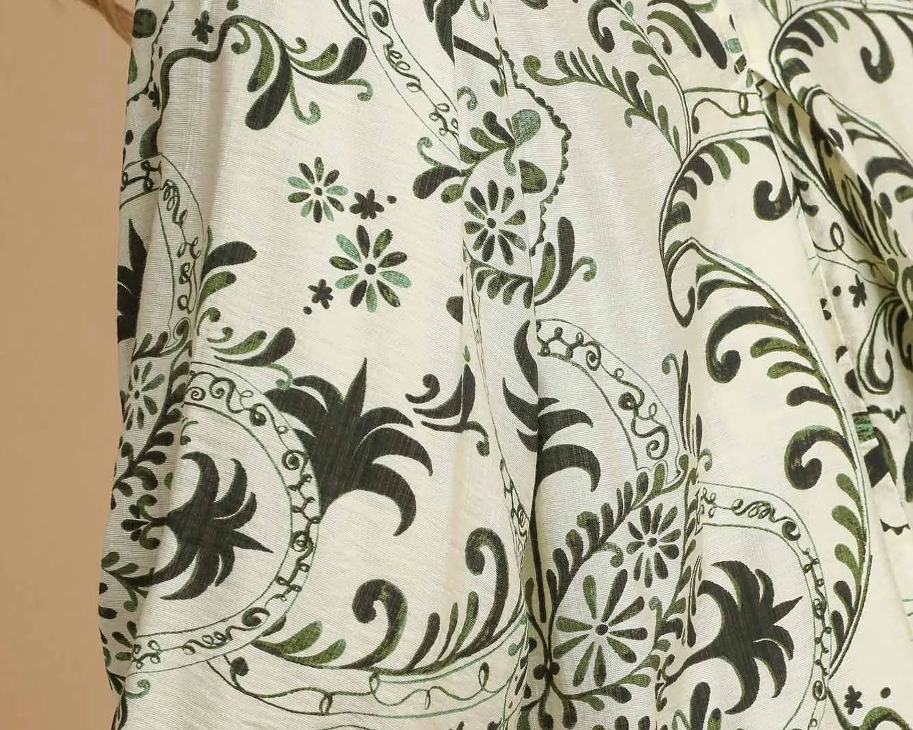 NEWYORKLISTED STYLE COLLECTION: Woman wearing a patterned blouse with green and black designs on a beige background