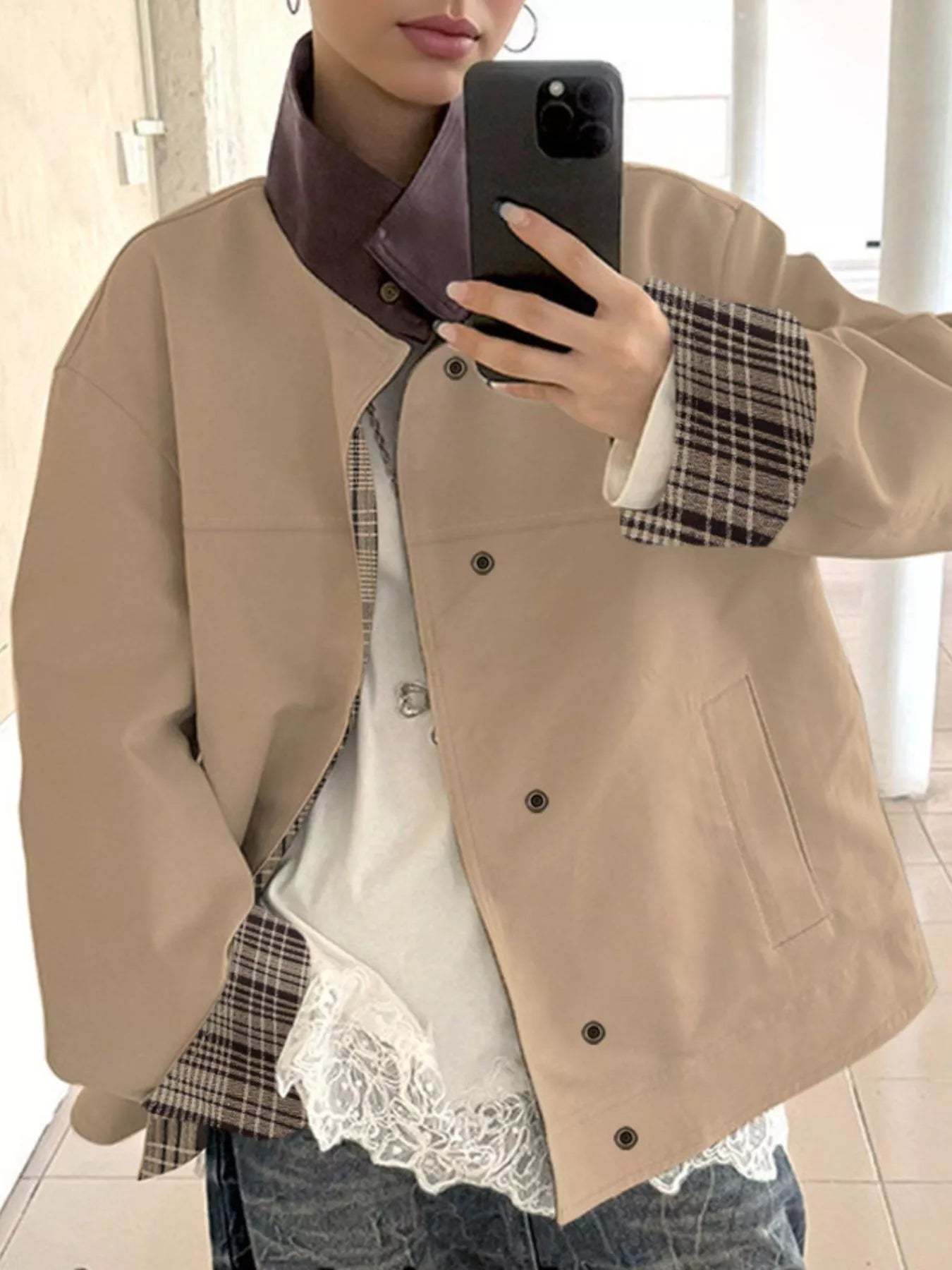 NEWYORKLISTED STYLE COLLECTION Person wearing a beige jacket over a plaid shirt with lace trim, holding a phone.