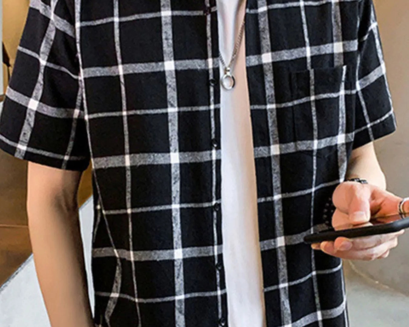 NEWYORKLISTED ATLAS MEN'S COLLECTION: Person wearing a black and white checkered shirt over a white t-shirt, holding a phone.