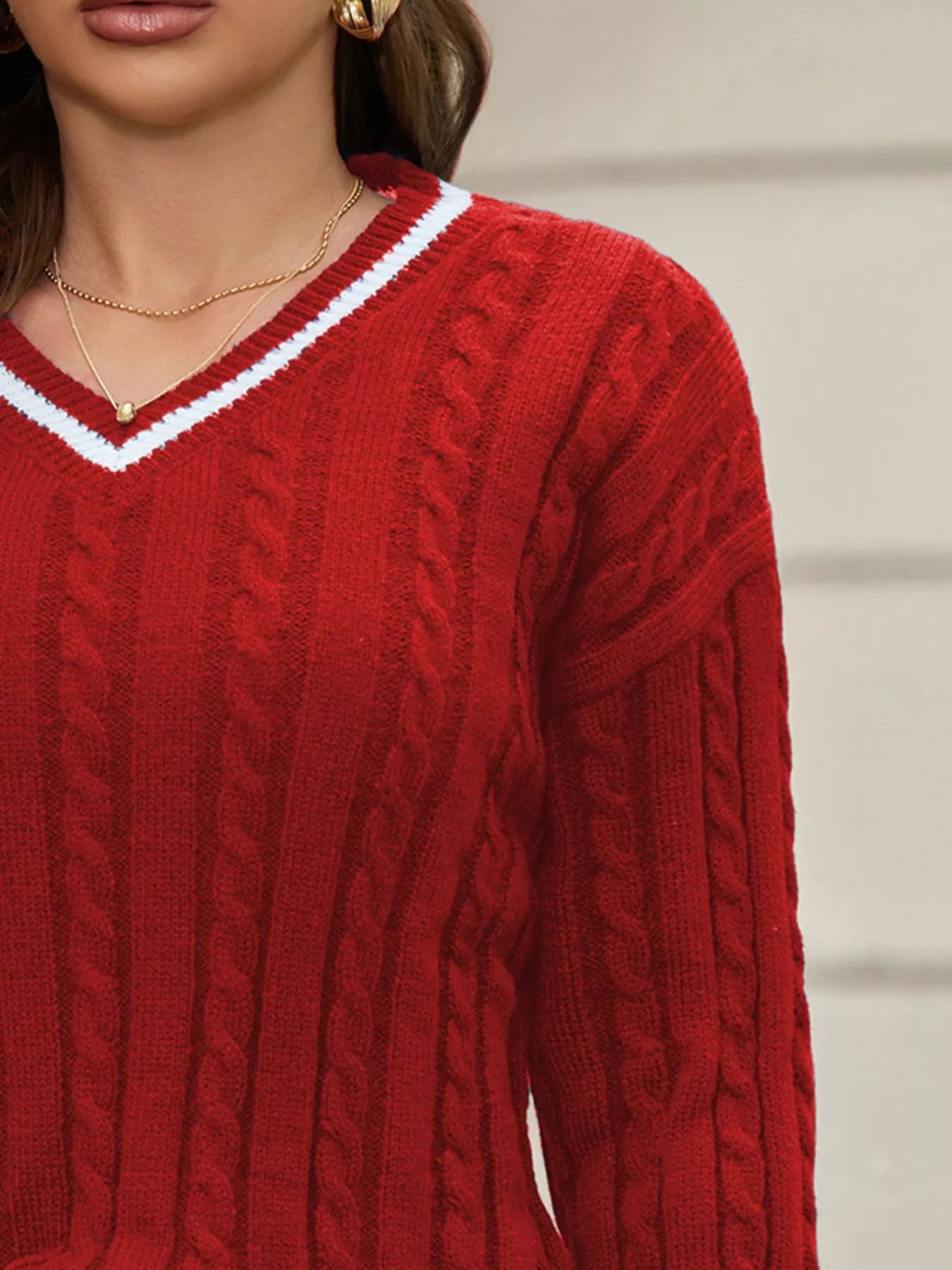 NEWYORKLSITED STYLE COLLECTION: Close-up of a person wearing a red cable knit sweater with a blurred background