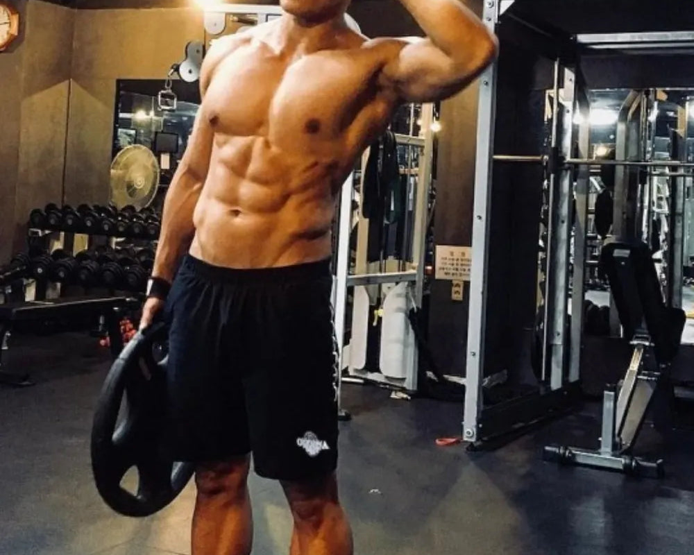 NEWYORKLISTED ATLAS MEN's COLLECTION: Muscular man posing in a gym holding a disc wearing NEWYORKLISTED ATLAS shorts