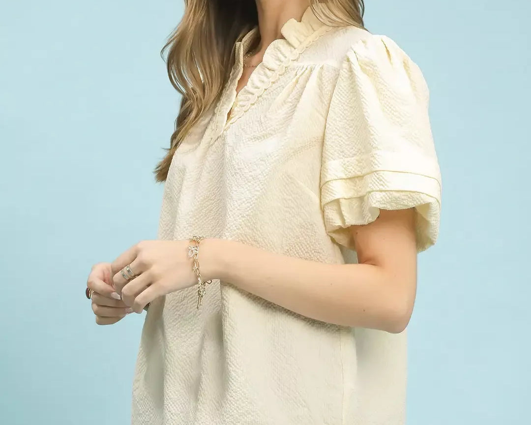 NEWYORKLISTED Style Collection: Woman wearing a cream blouse with ruffled sleeves against a light blue background