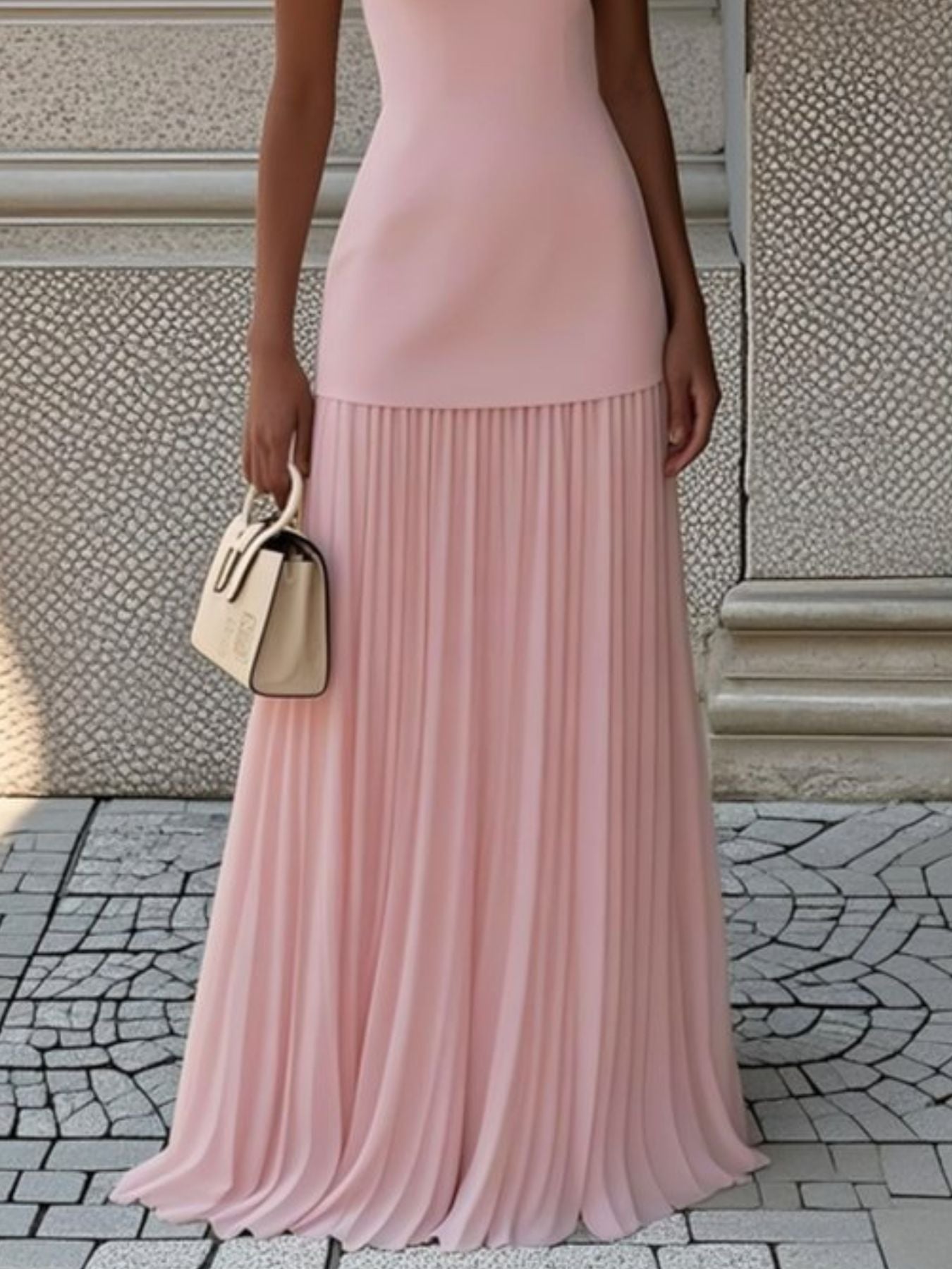 NEWYORKLISTED STYLE COLLECTION: Person wearing a pink pleated dress holding a beige handbag on a stone pavement.