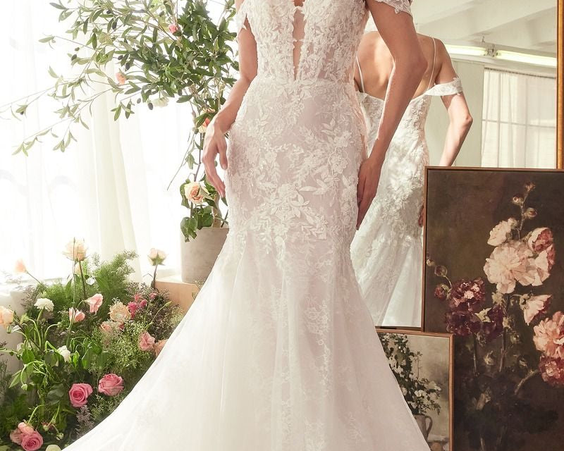 NEWYORKLISTED ELEGANT BRIDE COLLECTION: Woman in a white wedding dress standing in a decorated room with flowers and mirrors.